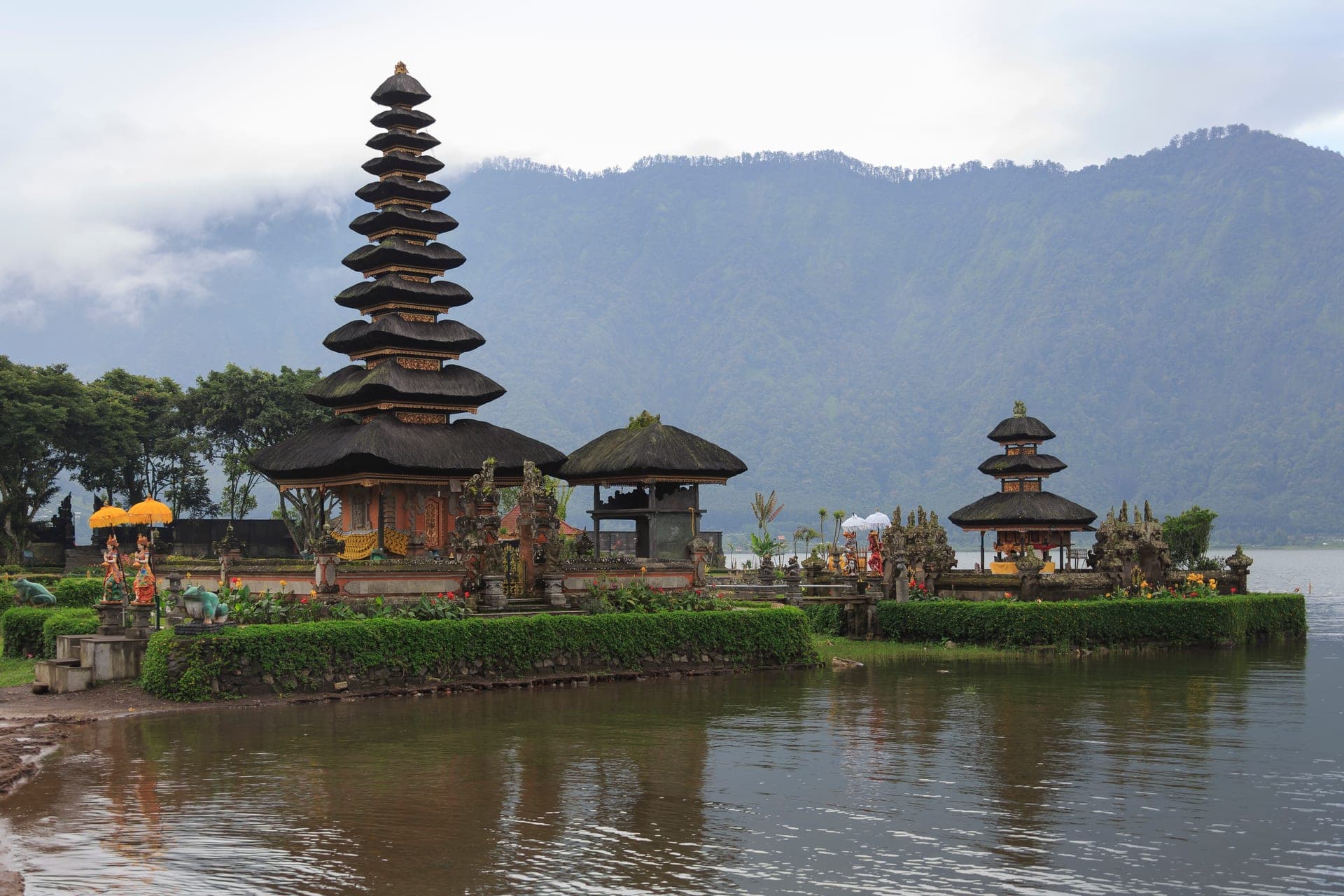 The tiered thatched shrines of Pura Ulun Danu Bratan sitting out on Lake Bratan in Bali, with cloud-covered volcanic ridges behind